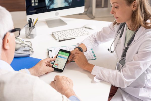 Young nutritionist in whitecoat showing senior patient smartphone with his new improved health indicators on its screen during consultation